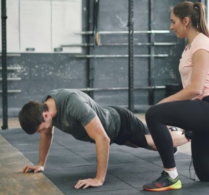 Strong guy is doing push-ups in sports gym while trainer young woman is speaking motivating student. Healthy activity, lifestyle and sports concept.